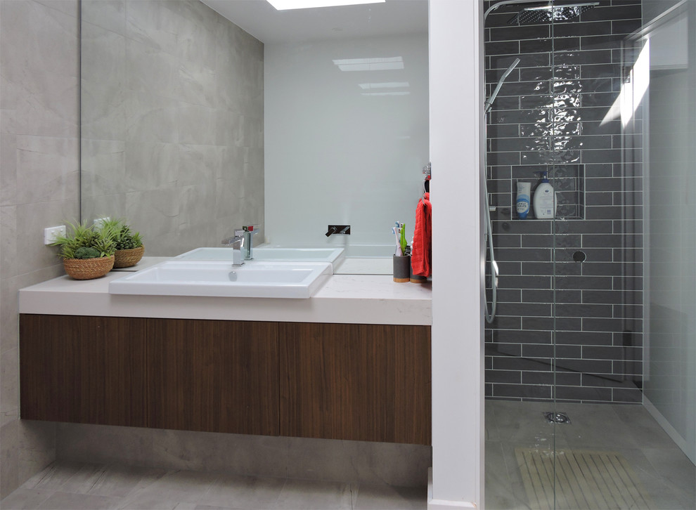 Photo of a mid-sized contemporary kids bathroom in Melbourne with furniture-like cabinets, dark wood cabinets, a drop-in tub, a double shower, a wall-mount toilet, gray tile, ceramic tile, beige walls, concrete floors, a vessel sink and engineered quartz benchtops.