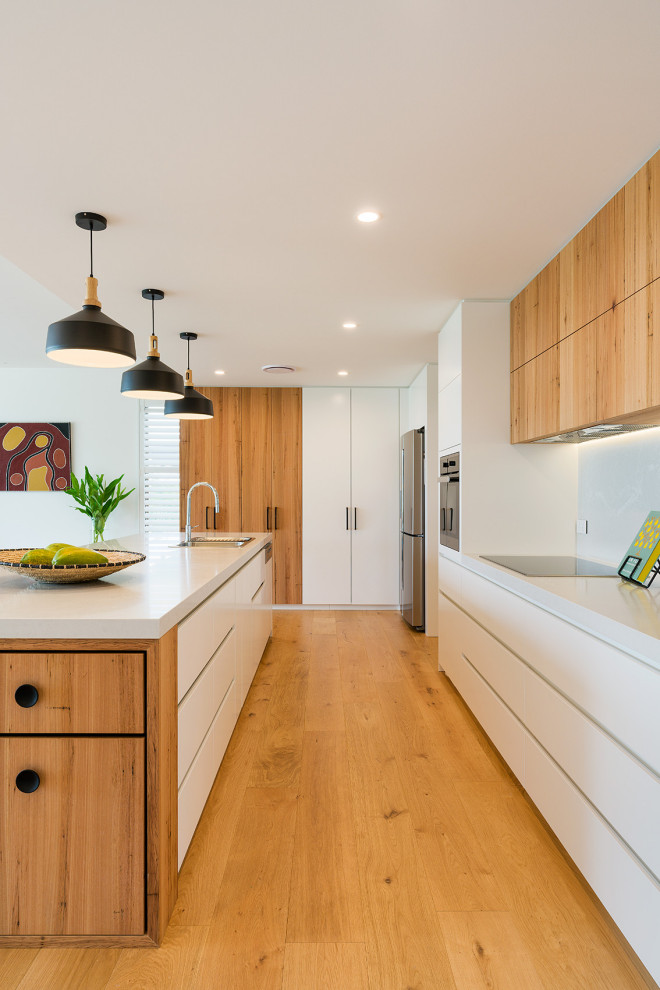 Photo of a large contemporary galley kitchen in Other with a drop-in sink, flat-panel cabinets, white cabinets, white splashback, medium hardwood floors, with island, brown floor and white benchtop.