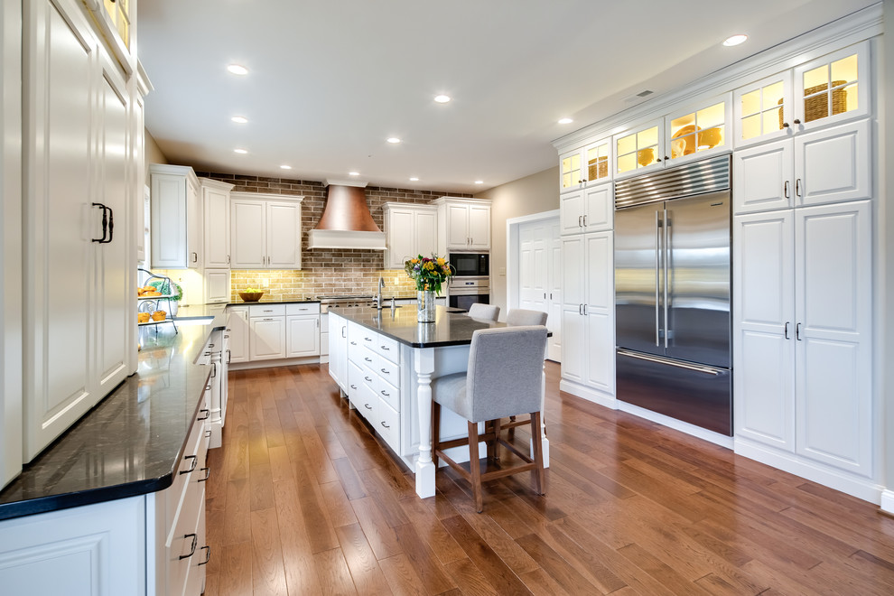 Photo of a large transitional l-shaped separate kitchen in Philadelphia with an undermount sink, raised-panel cabinets, white cabinets, quartz benchtops, brown splashback, ceramic splashback, stainless steel appliances, medium hardwood floors and with island.
