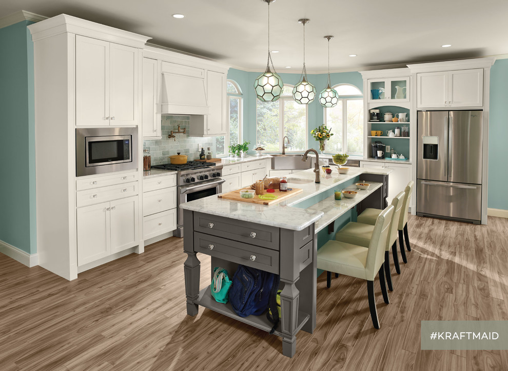 This is an example of a large traditional l-shaped eat-in kitchen in Detroit with recessed-panel cabinets, white cabinets, a farmhouse sink, grey splashback, stainless steel appliances, light hardwood floors and with island.
