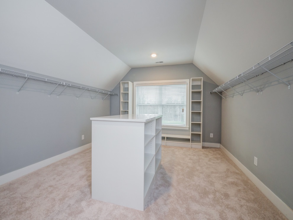 This is an example of an expansive gender-neutral walk-in wardrobe in Charlotte with carpet and vaulted.