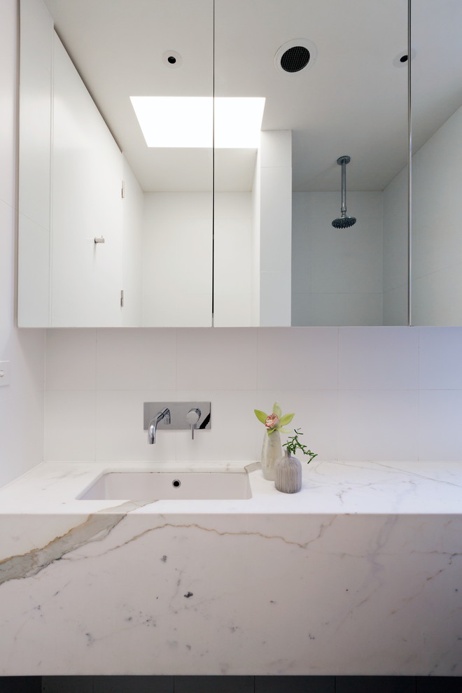 This is an example of a large contemporary master bathroom in Sydney with a drop-in sink, flat-panel cabinets, marble benchtops, an open shower, black tile, ceramic tile, white walls and ceramic floors.