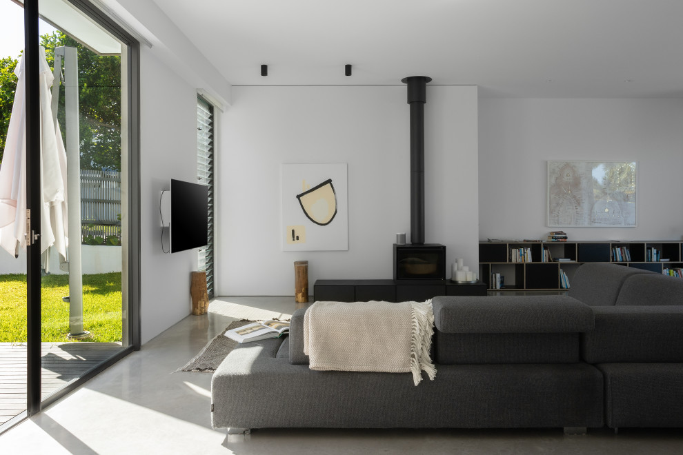 Immagine di un soggiorno minimal aperto con pareti bianche, pavimento in cemento e stufa a legna
