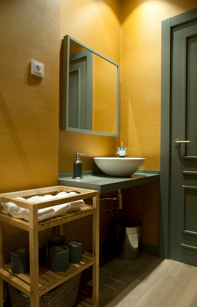 Photo of a scandinavian bathroom in Bilbao with open cabinets, light wood cabinets, a wall-mount toilet, yellow tile, yellow walls, laminate floors, a vessel sink, wood benchtops and grey floor.
