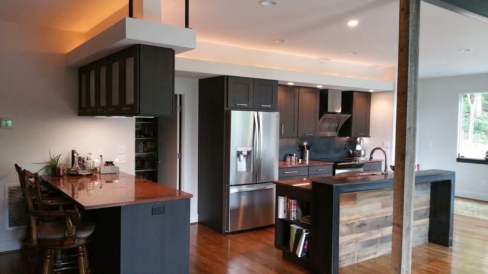 Example of a large mountain style l-shaped medium tone wood floor eat-in kitchen design with dark wood cabinets, black backsplash, stainless steel appliances and an island
