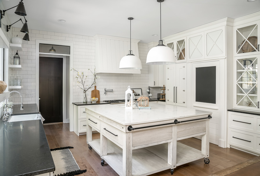 Design ideas for a country u-shaped kitchen in Chicago with a farmhouse sink, shaker cabinets, white cabinets, white splashback, subway tile splashback, medium hardwood floors, with island and brown floor.