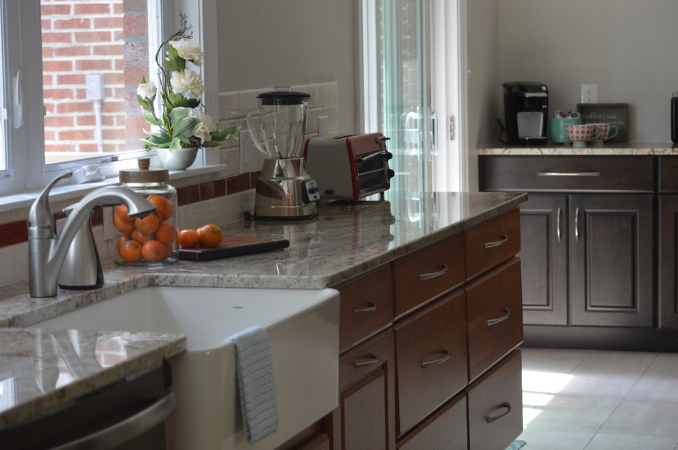 Eat-in kitchen - large transitional l-shaped porcelain tile and beige floor eat-in kitchen idea with a farmhouse sink, raised-panel cabinets, brown cabinets, granite countertops, white backsplash, ceramic backsplash, stainless steel appliances and a peninsula