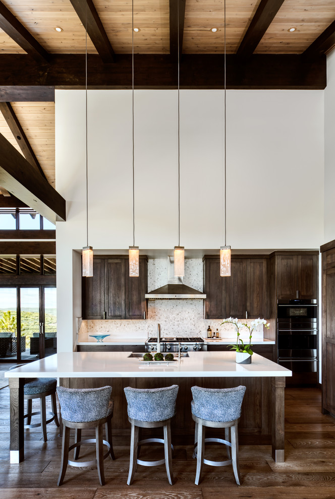 Inspiration for a mid-sized country l-shaped kitchen in Phoenix with a farmhouse sink, shaker cabinets, dark wood cabinets, white splashback, mosaic tile splashback, stainless steel appliances, dark hardwood floors, with island, brown floor and white benchtop.