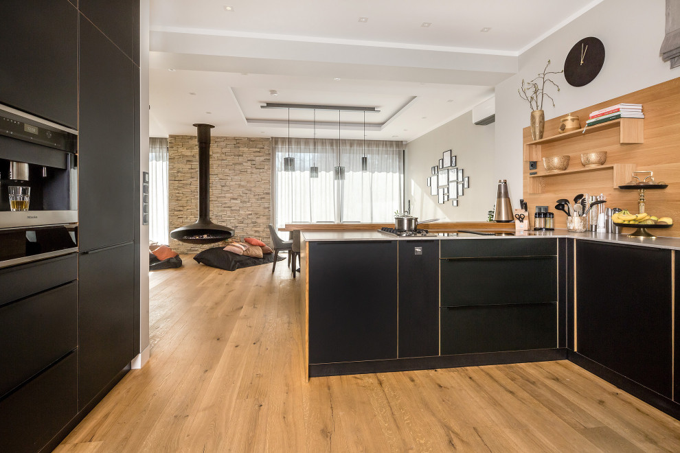 Küche in U-Form mit Einbauwaschbecken, Glasfronten, schwarzen Schränken, Mineralwerkstoff-Arbeitsplatte, Rückwand aus Holz, Küchengeräten aus Edelstahl, hellem Holzboden, braunem Boden und grauer Arbeitsplatte in Berlin