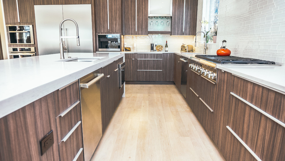 This is an example of a large contemporary open plan kitchen in Boston with an undermount sink, flat-panel cabinets, brown cabinets, quartzite benchtops, white splashback, glass tile splashback, stainless steel appliances, light hardwood floors and with island.