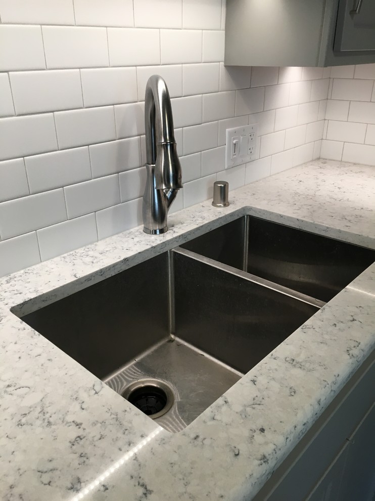 Inspiration for a mid-sized transitional l-shaped vinyl floor eat-in kitchen remodel with an undermount sink, shaker cabinets, quartz countertops, white backsplash and stainless steel appliances