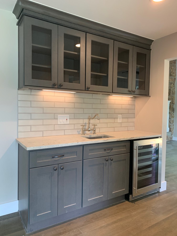 Mid-sized country u-shaped separate kitchen in Denver with an undermount sink, recessed-panel cabinets, grey cabinets, white splashback, ceramic splashback, brown floor, granite benchtops, stainless steel appliances, vinyl floors, with island and grey benchtop.