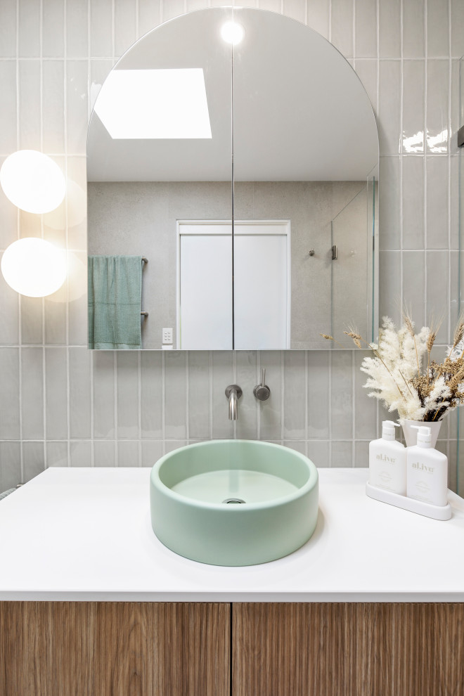 Bild på ett mellanstort funkis vit vitt badrum med dusch, med luckor med profilerade fronter, skåp i mellenmörkt trä, en öppen dusch, en toalettstol med hel cisternkåpa, grå kakel, porslinskakel, gröna väggar, klinkergolv i porslin, ett fristående handfat, bänkskiva i akrylsten, grått golv och med dusch som är öppen