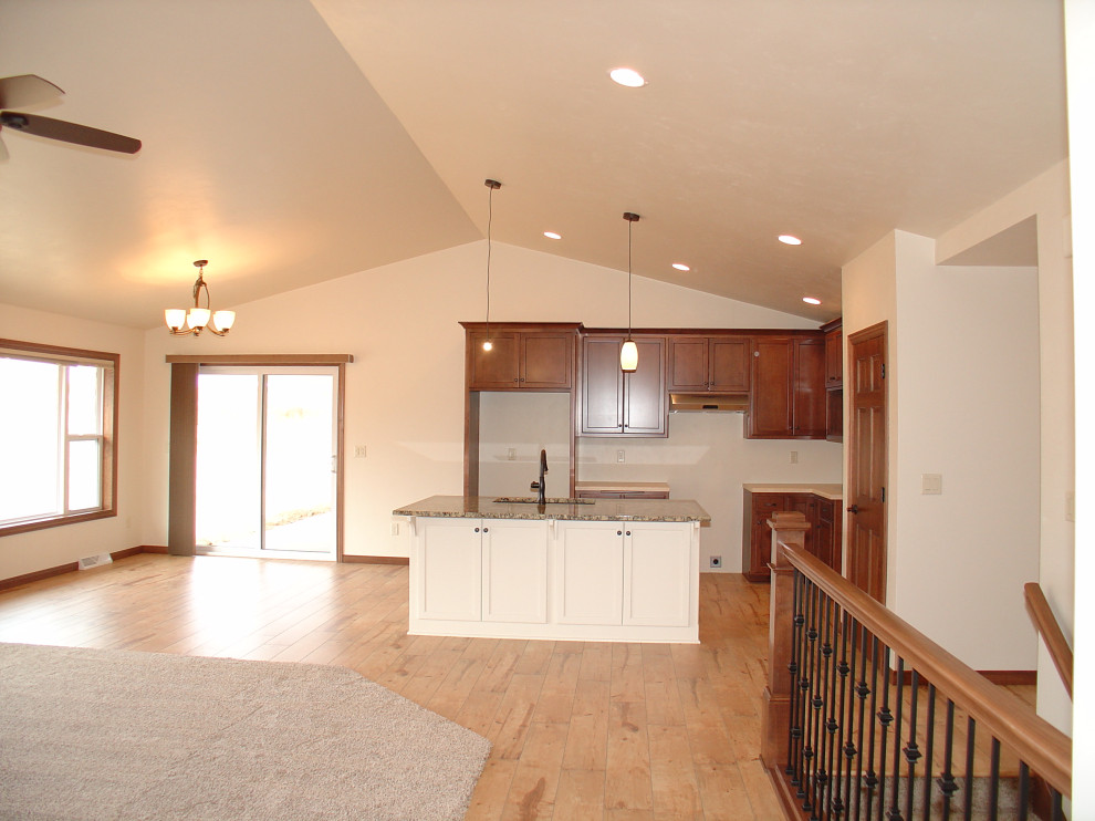 Large l-shaped light wood floor, brown floor and vaulted ceiling open concept kitchen photo with an undermount sink, recessed-panel cabinets, granite countertops and an island