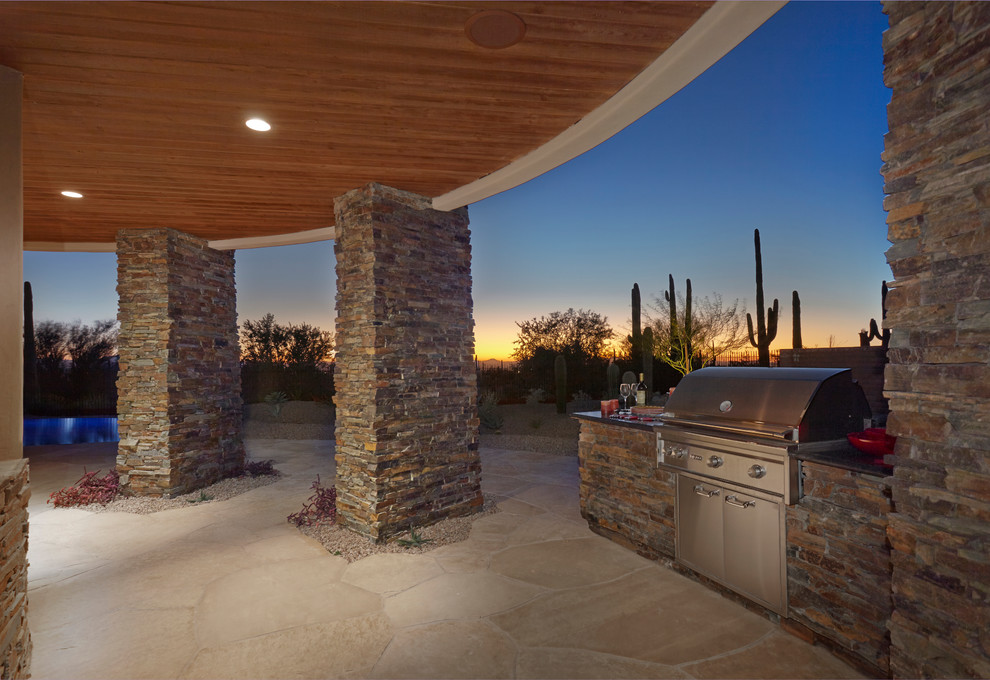 Design ideas for a large backyard patio in Phoenix with an outdoor kitchen, natural stone pavers and a roof extension.