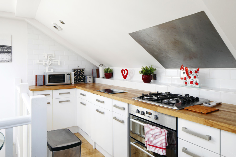 Photo of a small scandinavian l-shaped open plan kitchen in Sussex with flat-panel cabinets, white cabinets, white splashback, subway tile splashback, stainless steel appliances, medium hardwood floors, no island, a drop-in sink and wood benchtops.