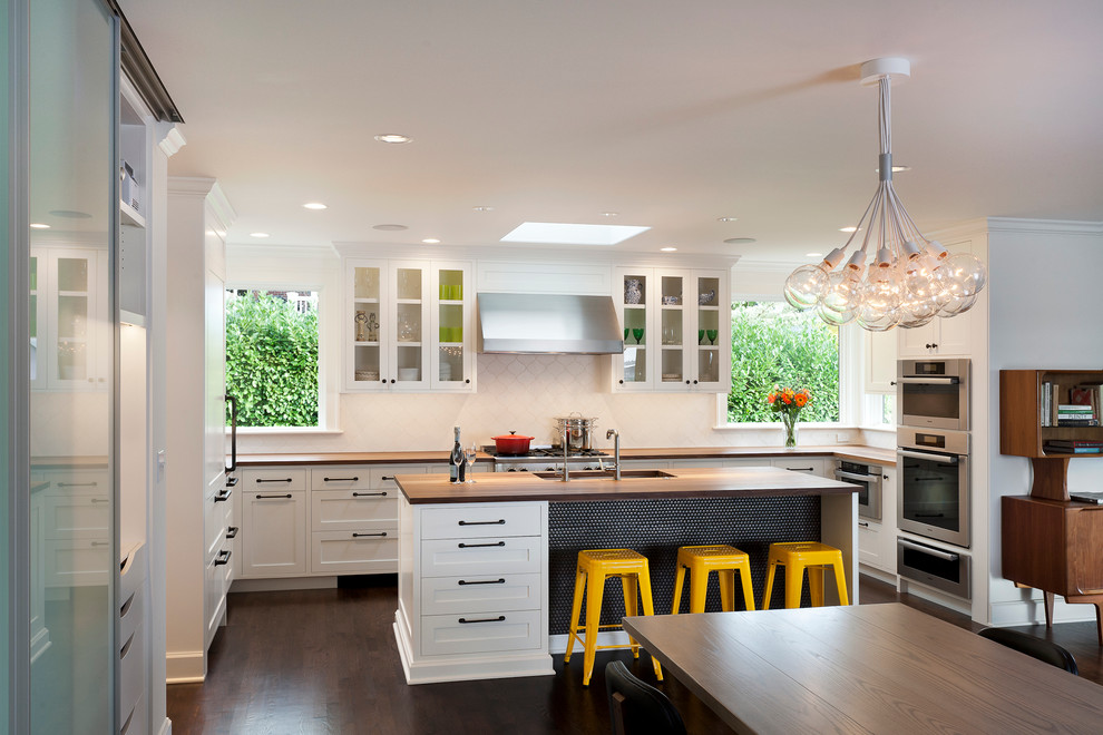 Example of a transitional u-shaped dark wood floor eat-in kitchen design in Seattle with an undermount sink, recessed-panel cabinets, white cabinets, wood countertops, white backsplash, ceramic backsplash, stainless steel appliances and an island