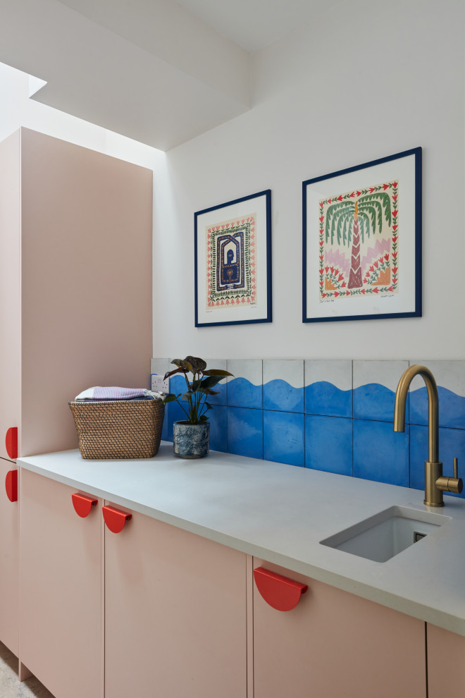 Design ideas for a small eclectic single-wall laundry room in London with a single-bowl sink, flat-panel cabinets, quartz benchtops, blue splashback, white walls, cork floors, an integrated washer and dryer and grey benchtop.