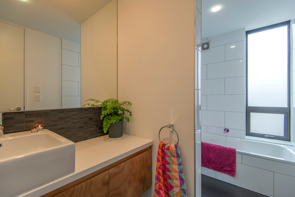 Photo of a small contemporary kids bathroom in Christchurch with a vessel sink, flat-panel cabinets, medium wood cabinets, engineered quartz benchtops, a drop-in tub, an alcove shower, black and white tile, ceramic tile, white walls and ceramic floors.