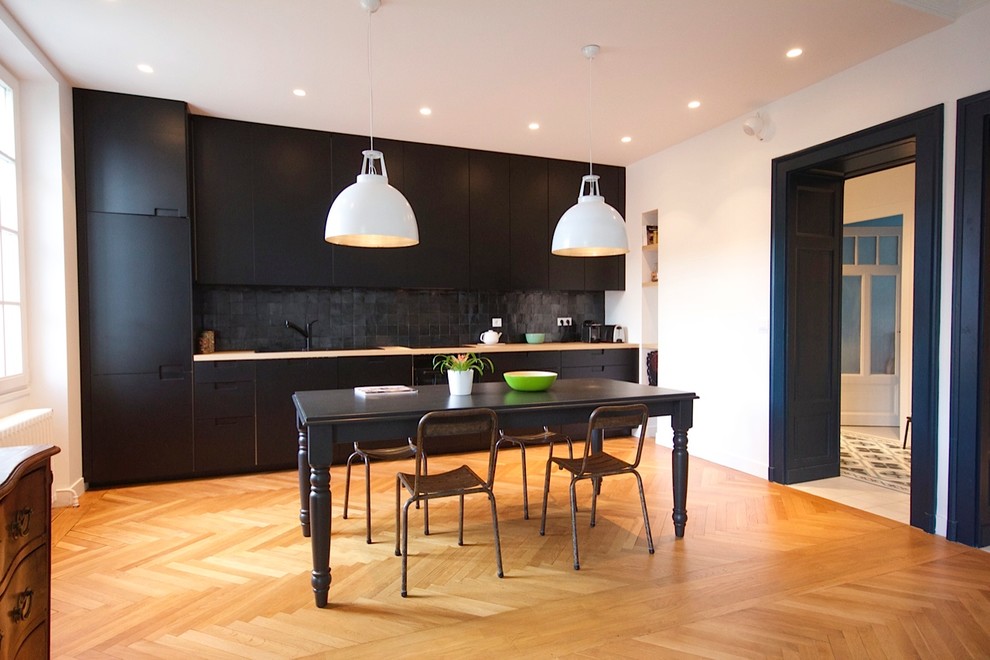 Photo of a contemporary single-wall eat-in kitchen in Toulouse with a single-bowl sink, black cabinets, laminate benchtops, black splashback, slate splashback, black appliances and light hardwood floors.