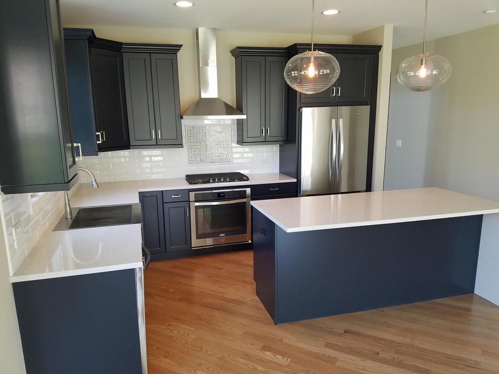Enclosed kitchen - mid-sized transitional l-shaped light wood floor and brown floor enclosed kitchen idea in Chicago with an undermount sink, shaker cabinets, blue cabinets, solid surface countertops, white backsplash, subway tile backsplash, stainless steel appliances and an island
