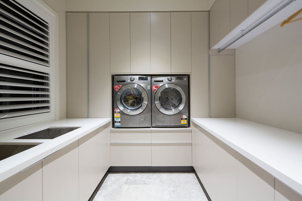 This is an example of a small contemporary u-shaped dedicated laundry room in Brisbane with a double-bowl sink, flat-panel cabinets, beige cabinets, quartz benchtops, beige walls, porcelain floors and a side-by-side washer and dryer.