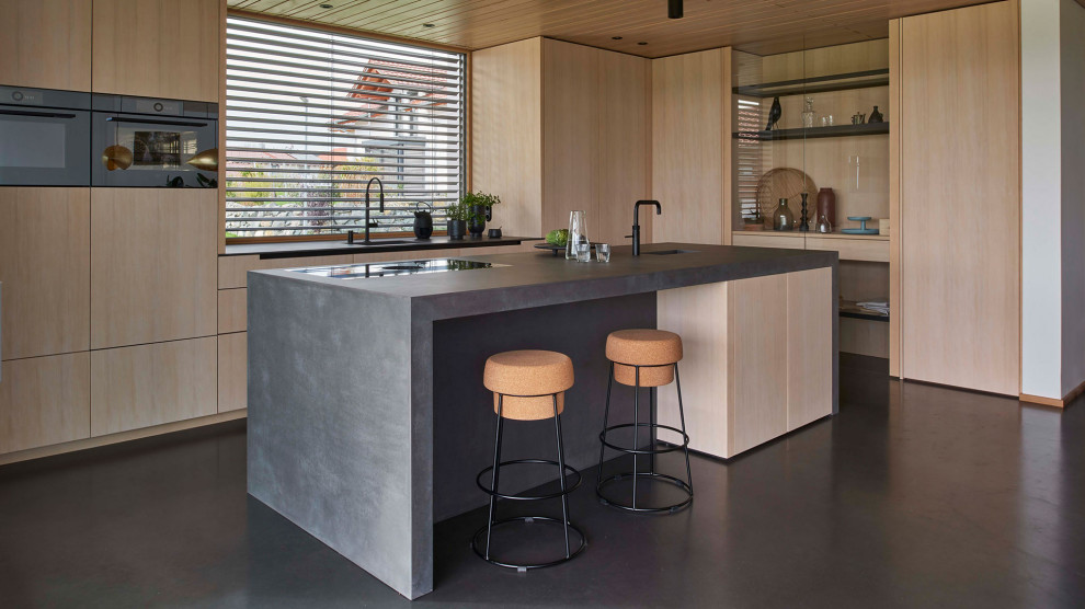 Moderne Küche mit hellen Holzschränken, Betonarbeitsplatte, Betonboden und schwarzer Arbeitsplatte in München