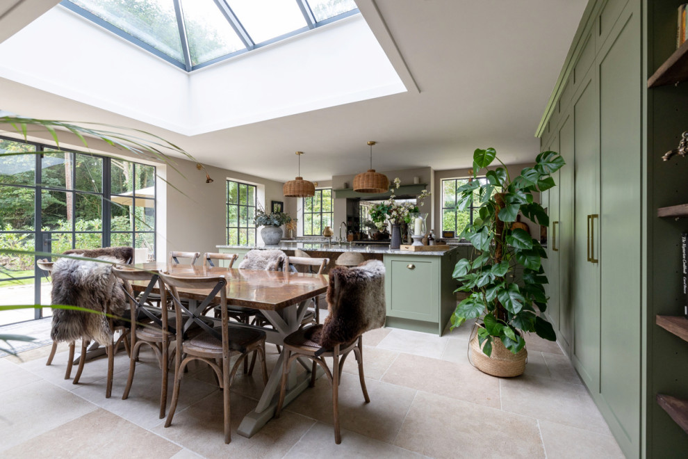 Photo of a large country l-shaped open plan kitchen in Gloucestershire with a farmhouse sink, shaker cabinets, green cabinets, granite benchtops, mirror splashback, panelled appliances, limestone floors, with island, beige floor and multi-coloured benchtop.