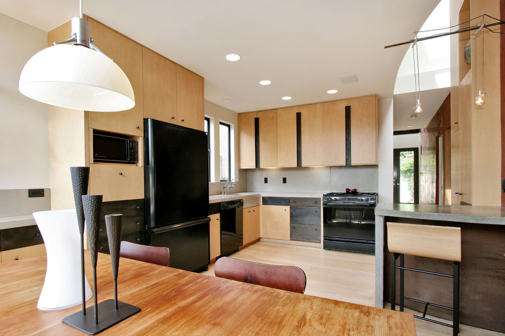 This is an example of a modern l-shaped kitchen in San Francisco with black appliances, concrete benchtops, flat-panel cabinets and light wood cabinets.