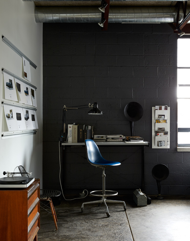 Photo of an industrial home office in New York with black walls, concrete floors, a freestanding desk and grey floor.