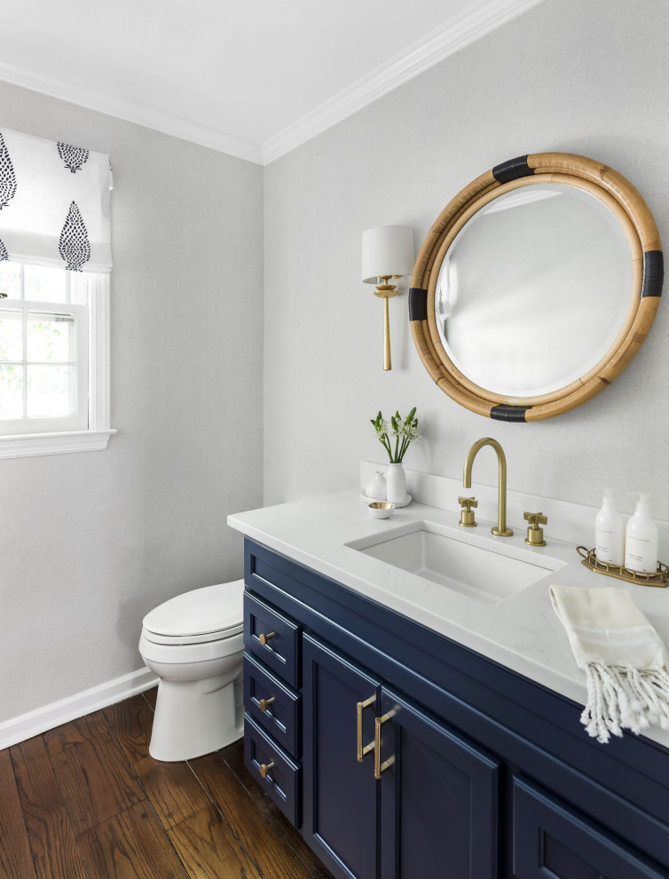 Transitional powder room in New York with recessed-panel cabinets, blue cabinets, grey walls, dark hardwood floors, an undermount sink, brown floor, white benchtops and a built-in vanity.