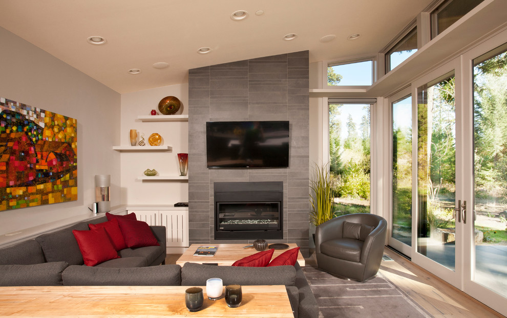 Esempio di un soggiorno minimalista di medie dimensioni e aperto con parquet chiaro, camino classico, cornice del camino piastrellata e TV a parete
