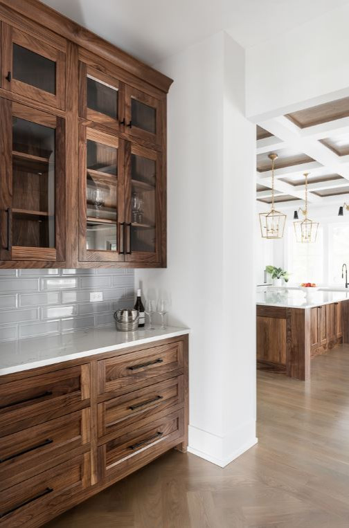 Photo of a large country galley wet bar in Chicago with shaker cabinets, medium wood cabinets, quartz benchtops, grey splashback, subway tile splashback, white benchtop, an undermount sink, light hardwood floors and brown floor.