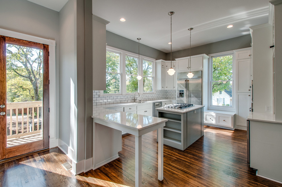 Photo of a mid-sized traditional u-shaped separate kitchen in Nashville with an undermount sink, shaker cabinets, white cabinets, quartz benchtops, white splashback, subway tile splashback, stainless steel appliances, dark hardwood floors and with island.