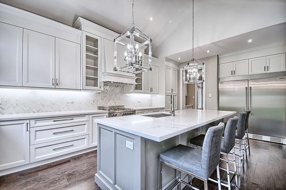 Inspiration for a large arts and crafts u-shaped separate kitchen in Toronto with an undermount sink, shaker cabinets, white cabinets, quartzite benchtops, white splashback, mosaic tile splashback, stainless steel appliances, medium hardwood floors, with island and brown floor.