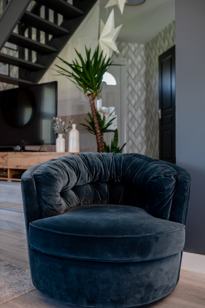 Modelo de salón abierto nórdico de tamaño medio con paredes grises, suelo de madera clara, estufa de leña, televisor independiente y suelo gris
