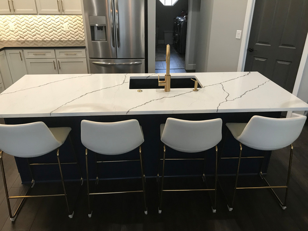 This is an example of an expansive transitional l-shaped open plan kitchen in Baltimore with an undermount sink, shaker cabinets, white cabinets, quartz benchtops, white splashback, marble splashback, stainless steel appliances, vinyl floors, with island, brown floor and multi-coloured benchtop.