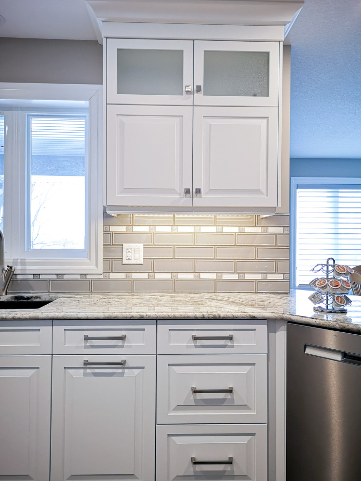 Mid-sized transitional u-shaped light wood floor and brown floor enclosed kitchen photo in Toronto with an undermount sink, raised-panel cabinets, white cabinets, granite countertops, beige backsplash, glass tile backsplash, stainless steel appliances, a peninsula and gray countertops