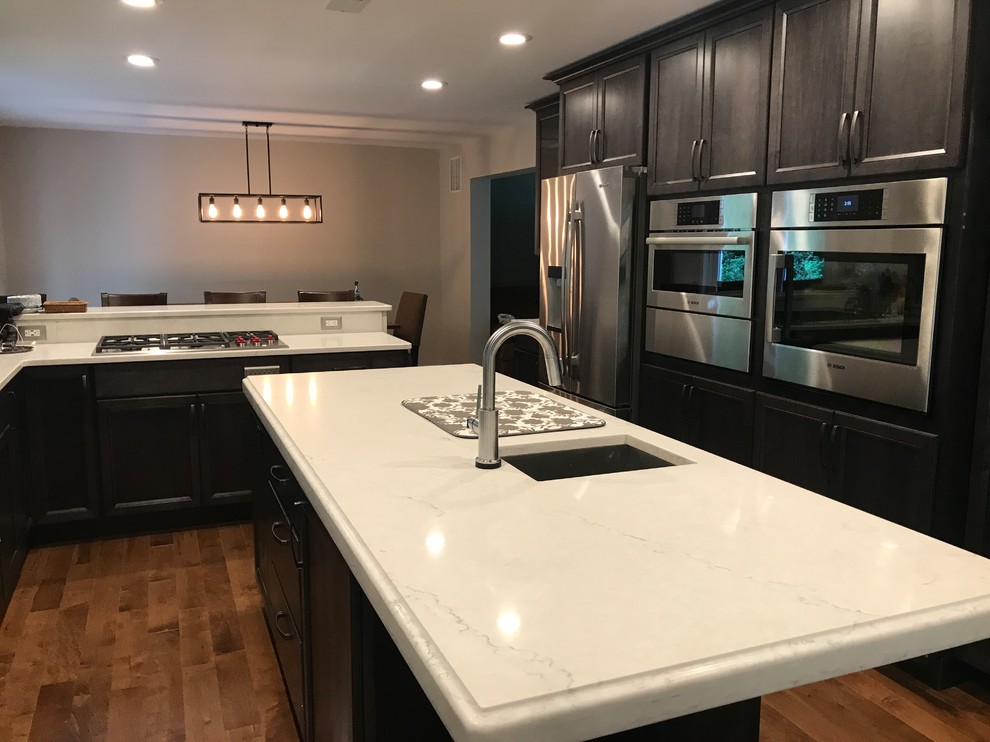 Photo of a large transitional u-shaped open plan kitchen in DC Metro with an undermount sink, flat-panel cabinets, dark wood cabinets, quartz benchtops, white splashback, stone slab splashback, stainless steel appliances, medium hardwood floors, with island and brown floor.