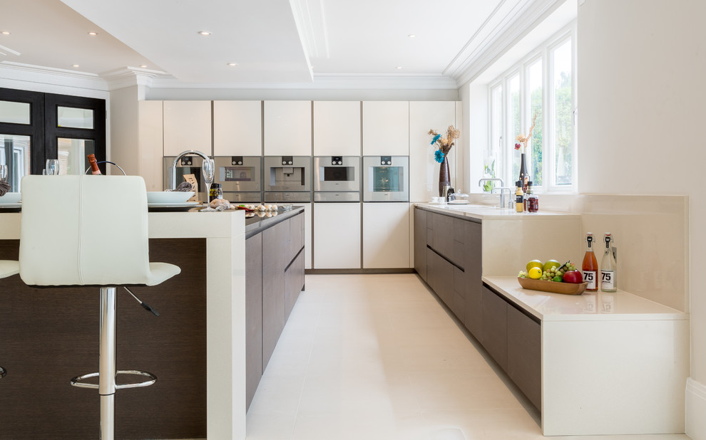 Large contemporary u-shaped kitchen in Berkshire with a drop-in sink, flat-panel cabinets, beige cabinets, solid surface benchtops, stainless steel appliances and with island.