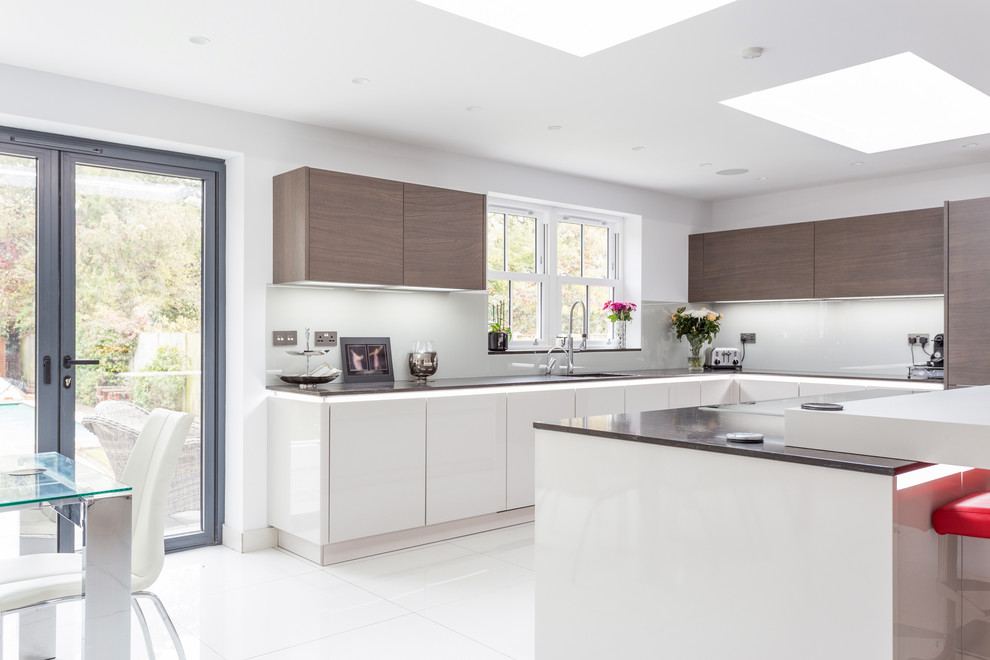 This is an example of a large l-shaped open plan kitchen in London with glass-front cabinets, dark wood cabinets, granite benchtops, grey splashback, glass sheet splashback and with island.
