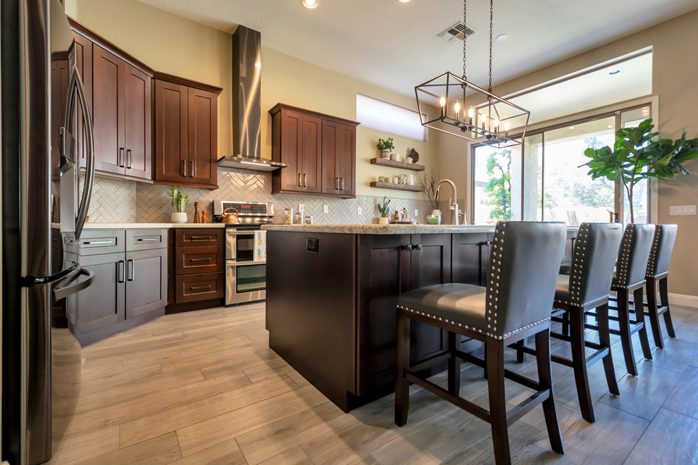 Open concept kitchen - mid-sized transitional l-shaped porcelain tile and brown floor open concept kitchen idea in Phoenix with a single-bowl sink, shaker cabinets, brown cabinets, granite countertops, gray backsplash, brick backsplash, stainless steel appliances, an island and multicolored countertops