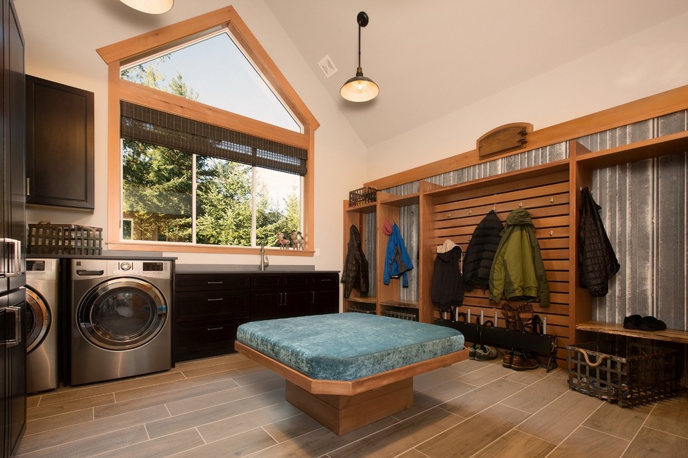 Photo of a mid-sized country utility room in Seattle with an undermount sink, raised-panel cabinets, dark wood cabinets, solid surface benchtops, grey walls, porcelain floors, a side-by-side washer and dryer and grey floor.