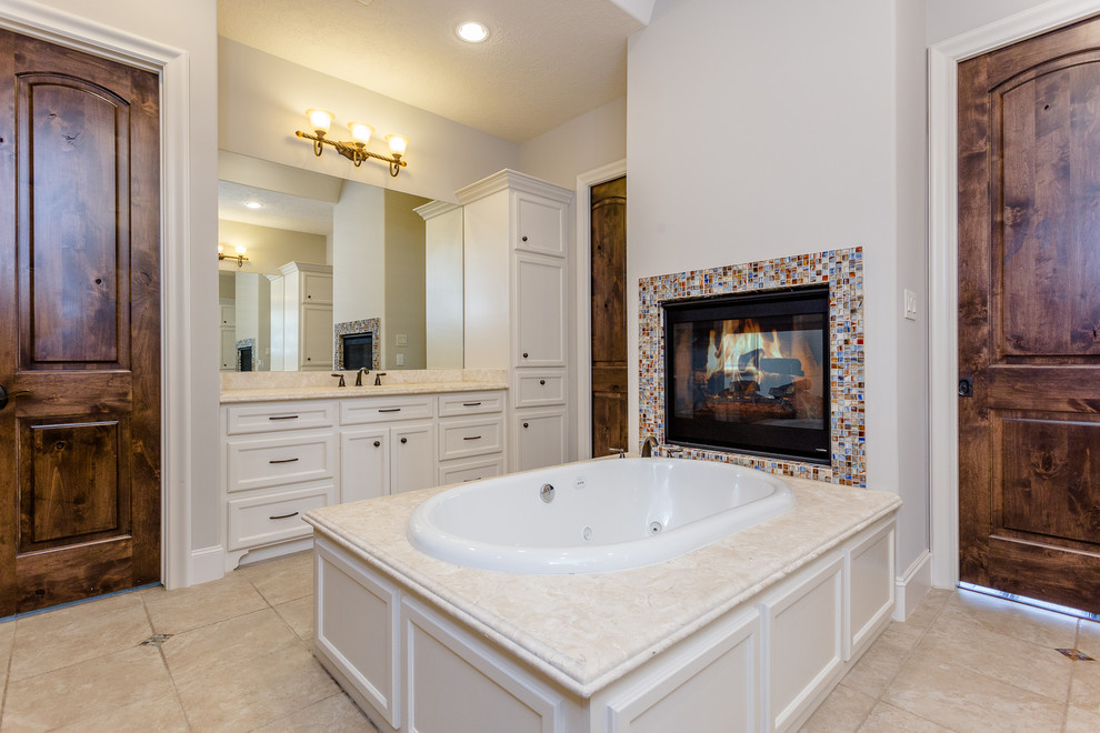 Design ideas for a large mediterranean master bathroom in Houston with recessed-panel cabinets, white cabinets, a drop-in tub, a curbless shower, a two-piece toilet, beige tile, travertine, beige walls, travertine floors, an undermount sink, granite benchtops, beige floor, an open shower and beige benchtops.