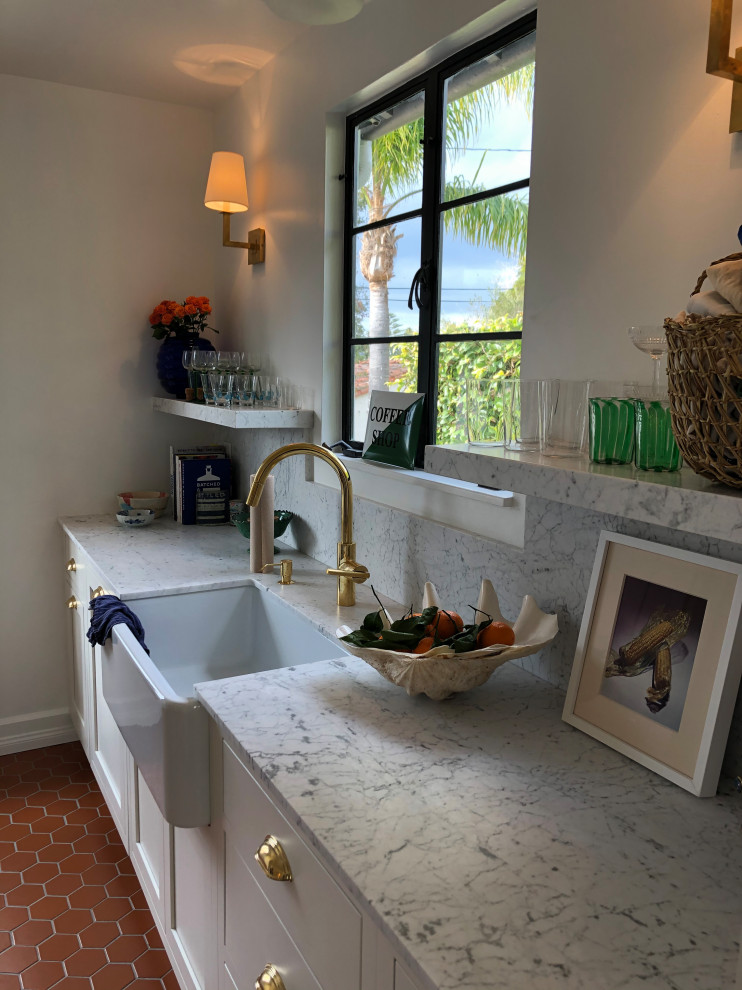 Inspiration for a small mediterranean galley separate kitchen in Santa Barbara with a farmhouse sink, shaker cabinets, white cabinets, marble benchtops, white splashback, marble splashback, stainless steel appliances, terra-cotta floors, no island, red floor and white benchtop.
