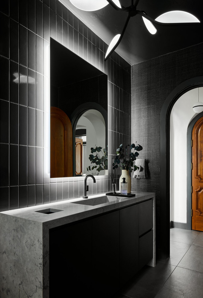 Bild på ett funkis grå grått toalett, med släta luckor, svarta skåp, svart kakel, keramikplattor, svarta väggar, ett integrerad handfat, bänkskiva i kalksten och grått golv
