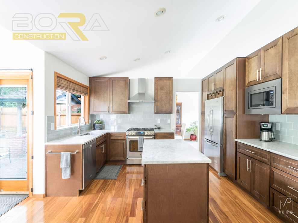 Inspiration for a mid-sized transitional l-shaped medium tone wood floor and brown floor eat-in kitchen remodel with an undermount sink, shaker cabinets, medium tone wood cabinets, quartz countertops, gray backsplash, ceramic backsplash, stainless steel appliances and an island