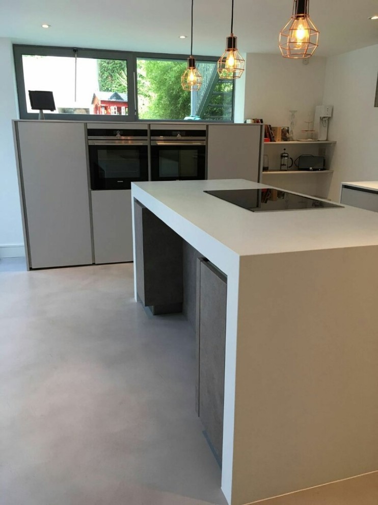Photo of a medium sized contemporary l-shaped enclosed kitchen in London with a submerged sink, flat-panel cabinets, grey cabinets, wood worktops, white splashback, stone slab splashback, black appliances, vinyl flooring and an island.
