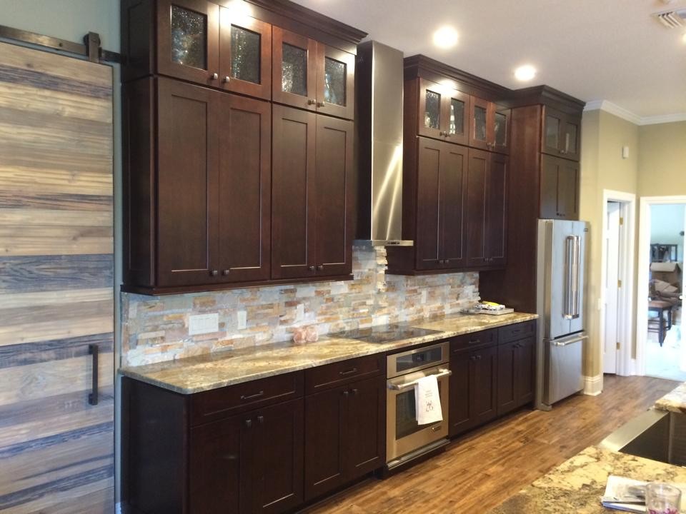 Large transitional galley eat-in kitchen in Tampa with recessed-panel cabinets, dark wood cabinets, granite benchtops, multi-coloured splashback, stone tile splashback, stainless steel appliances, medium hardwood floors, with island, brown floor and a farmhouse sink.