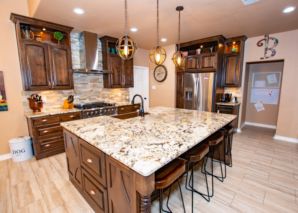 Example of a transitional porcelain tile and beige floor kitchen design in Austin with a farmhouse sink, raised-panel cabinets, dark wood cabinets, granite countertops, stone tile backsplash, stainless steel appliances and an island